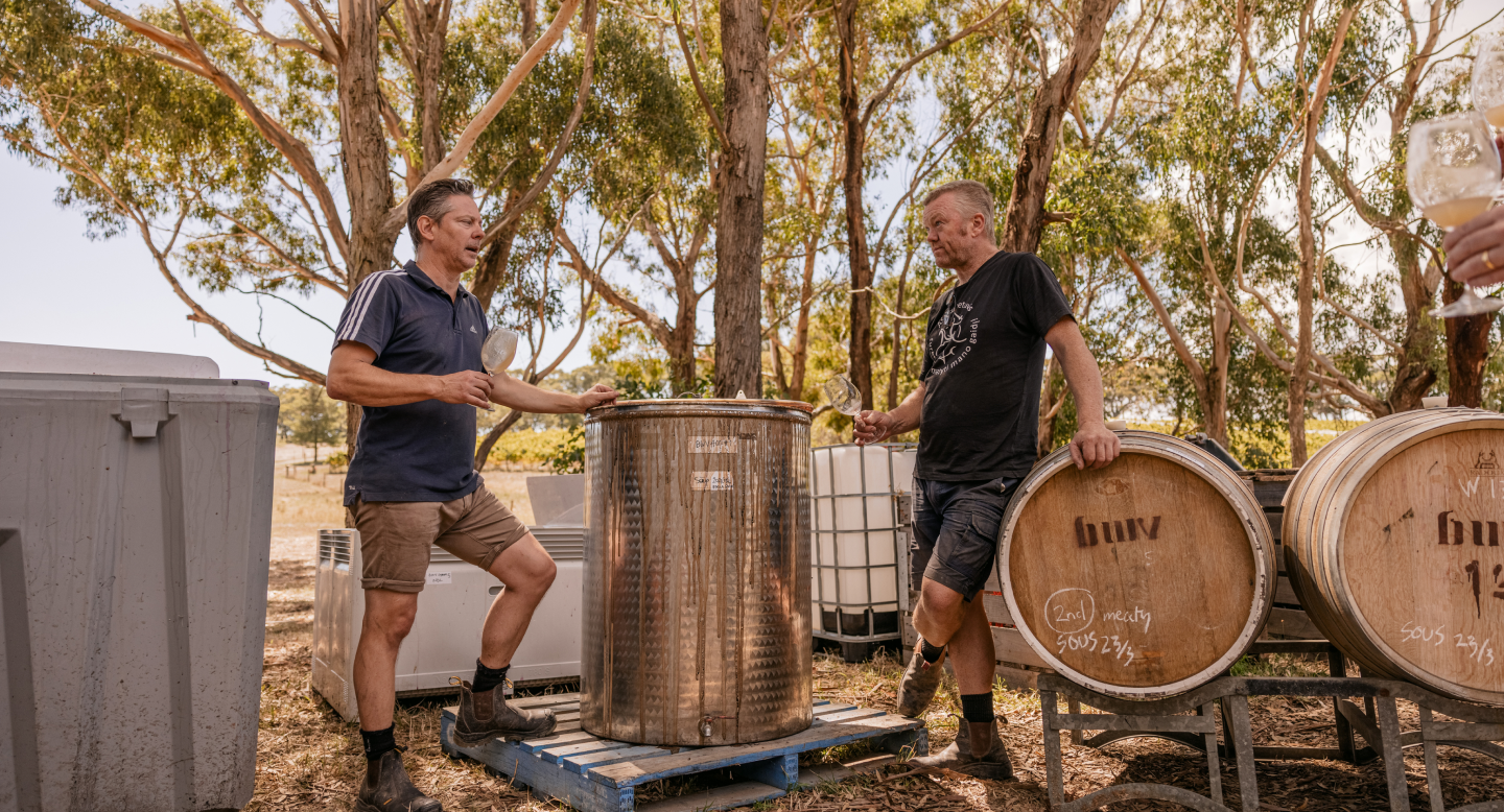 Damon and Dave enjoying wine outside among wine barrels